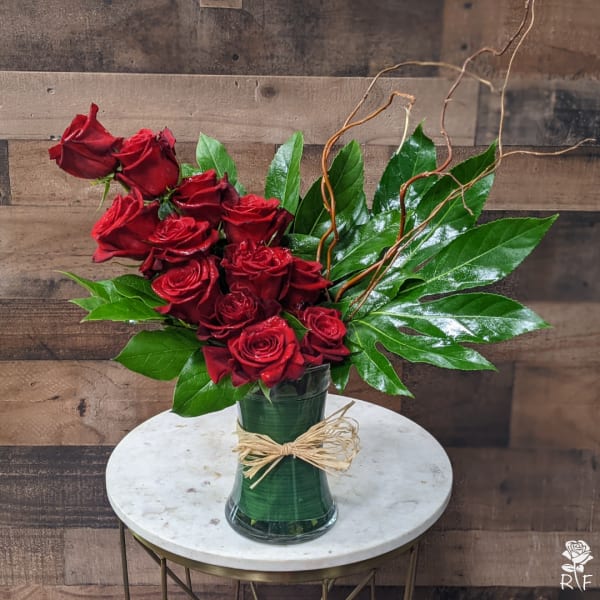 Red roses arranged in a clear glass vase with large green leaves