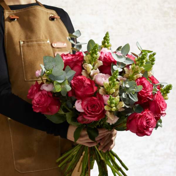 Handheld bouquet of red roses with pink blooms and eucalyptus