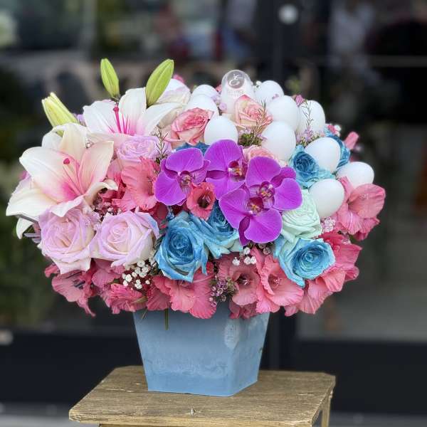 Colorful bouquet with lilies, roses, orchids, and white eggs in a blue vase