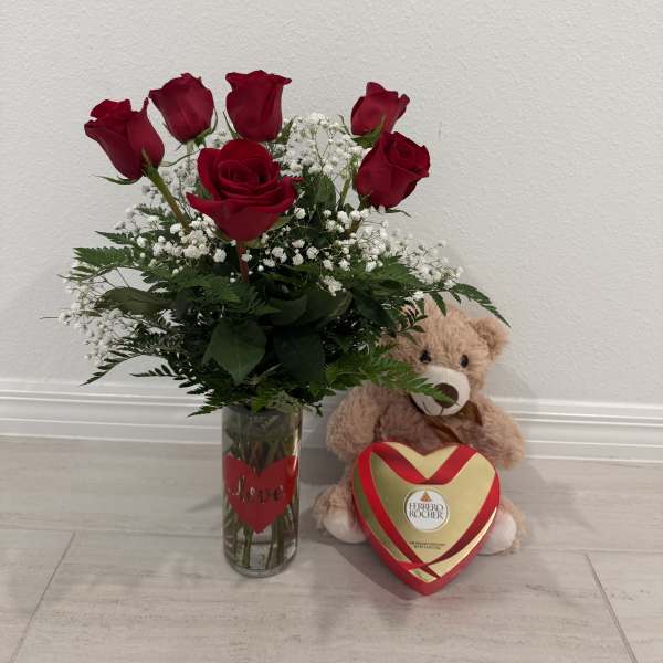 Red roses in a glass vase with a teddy bear and heart-shaped chocolate box