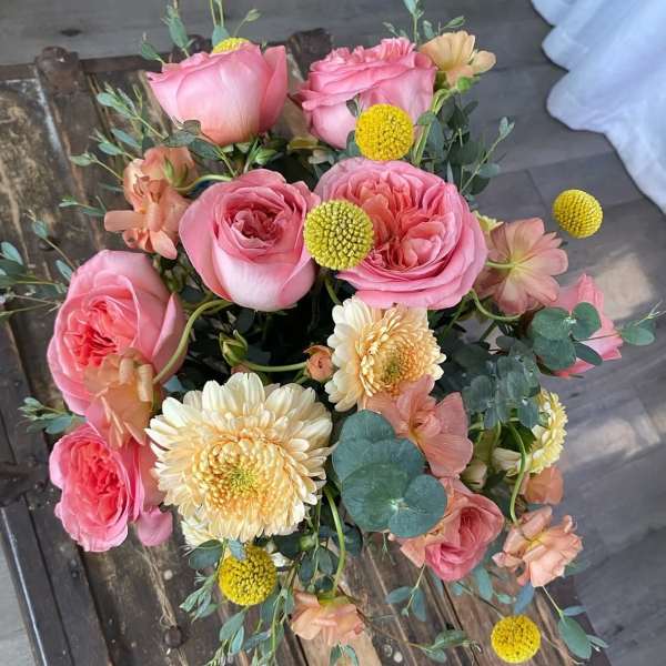 Pink roses with cream daisies and yellow button flowers in a loose bouquet