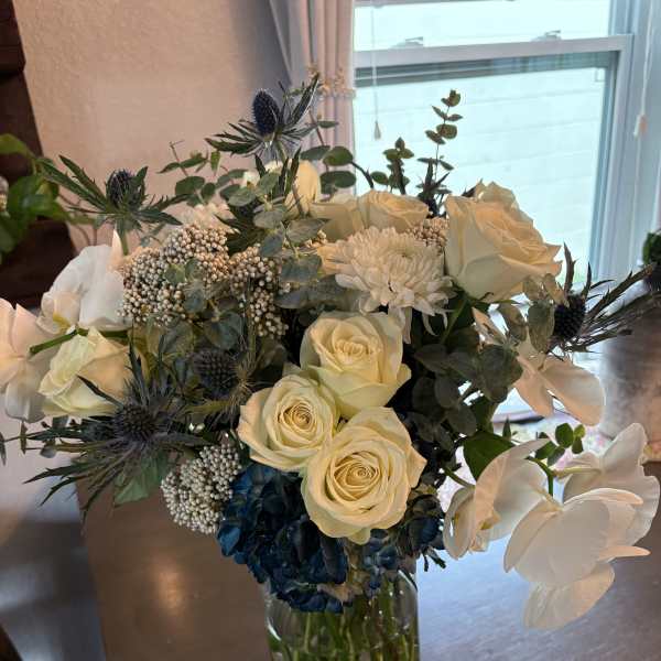 Bouquet of cream roses, white blooms, and blue thistles in a glass vase