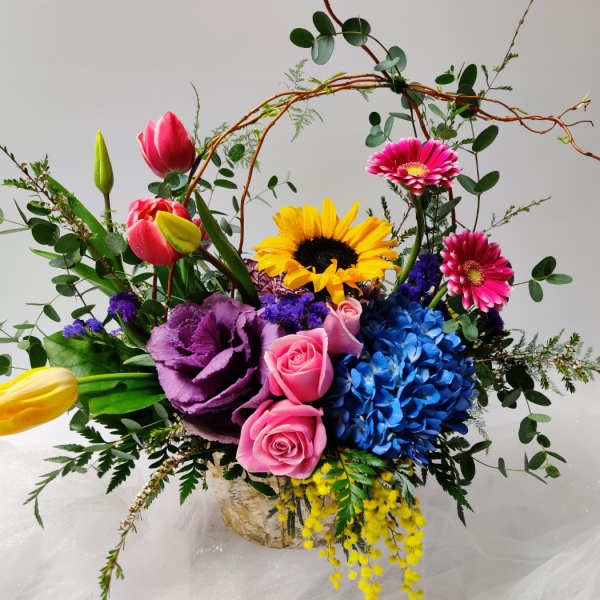 Colorful mixed bouquet with tulips, roses, sunflower, and hydrangea in a basket