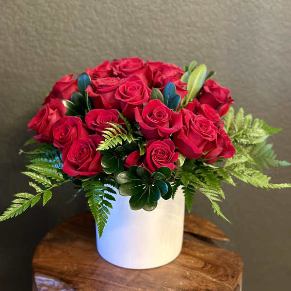 Red roses arranged in a white cylindrical vase with fern accents