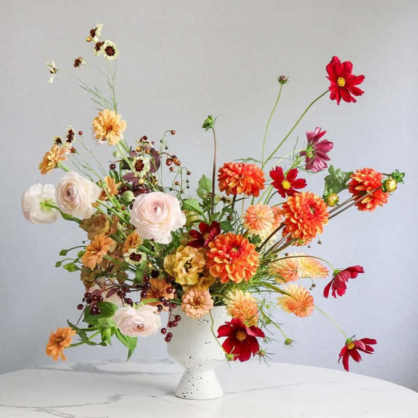 Loose bouquet of orange, red, and white flowers in a white vase