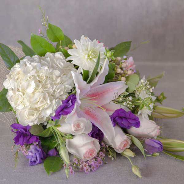 White and purple bouquet with lilies and roses on burlap wrap