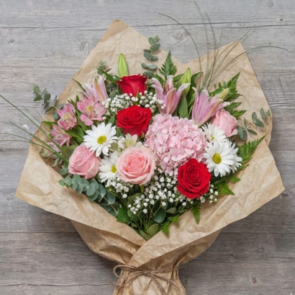Bouquet of red and pink roses with lilies and daisies in kraft paper