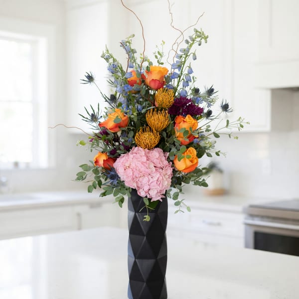 Tall bouquet of orange and pink flowers in a black vase
