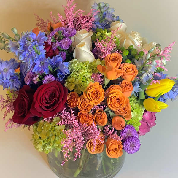 Mixed bouquet of roses, hydrangeas, and blue flowers in a glass vase