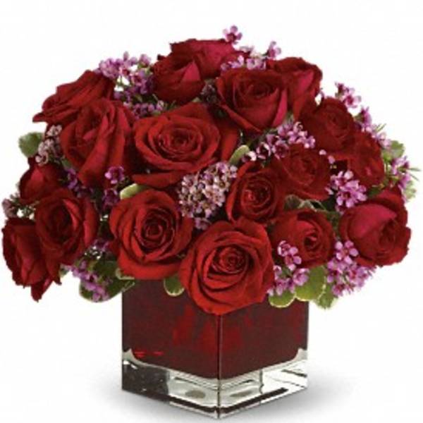 Red roses and purple filler flowers in a square glass vase