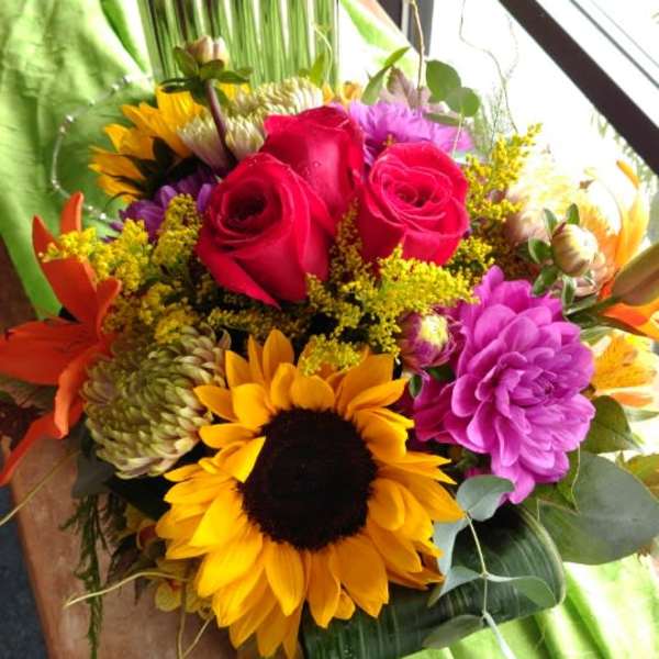 Bouquet of red roses, sunflowers, and purple blooms in a vase