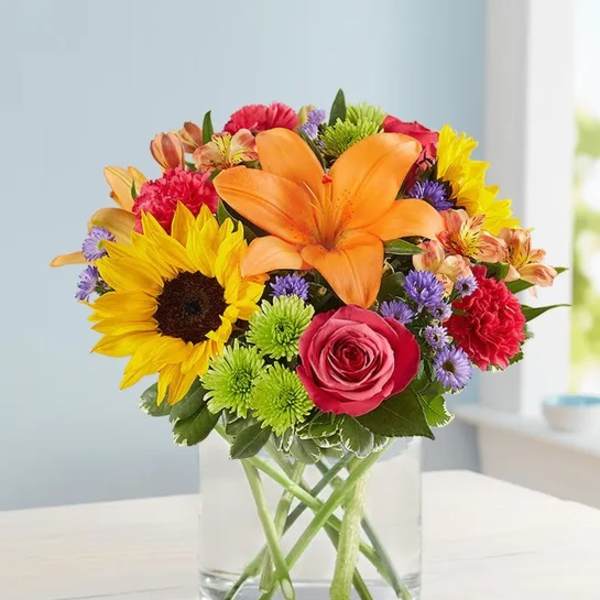 Colorful bouquet with sunflower, orange lily, and pink rose in a glass vase
