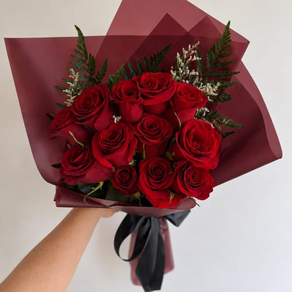 Handheld bouquet of red roses wrapped in burgundy paper