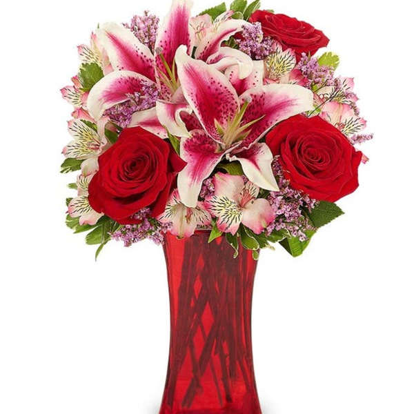 Red roses and pink lilies arranged in a red glass vase