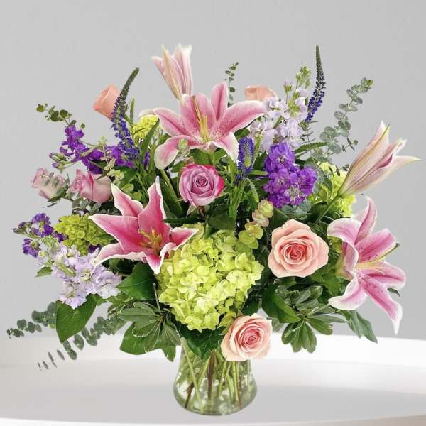 Mixed bouquet of pink lilies, roses, and purple flowers in a glass vase