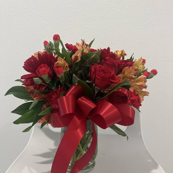 Red and orange mixed bouquet in a glass vase with a large red ribbon