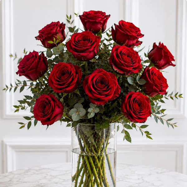 Red roses arranged in a clear glass vase with greenery