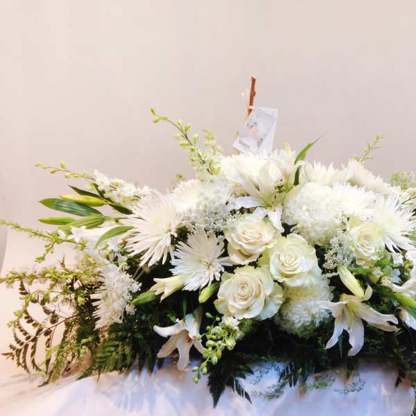 White floral casket spray with roses, lilies, and chrysanthemums