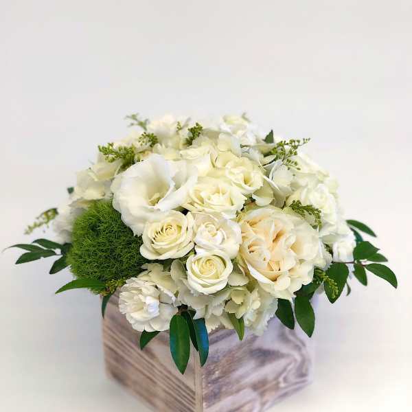 White floral arrangement in a wooden box with green accents
