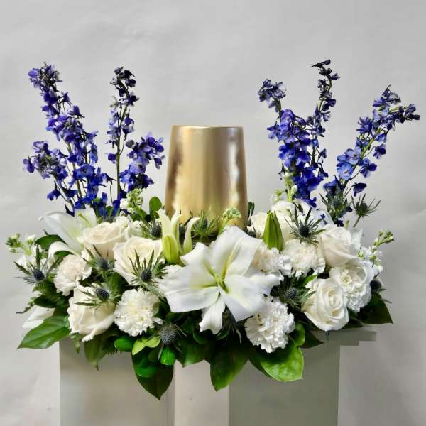 White floral arrangement with blue flowers around a gold vase