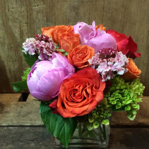 Bouquet of orange and pink roses with purple blooms in a glass vase