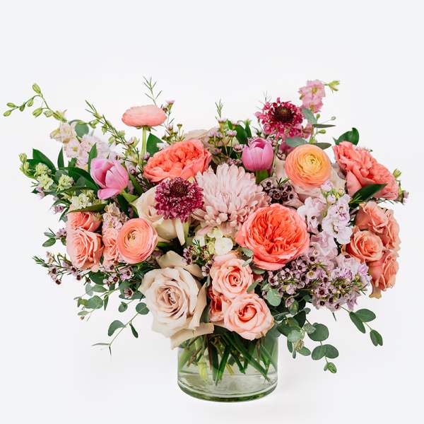 Mixed pink and peach flowers arranged in a clear glass vase