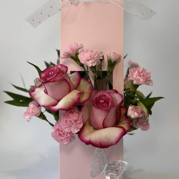 Pink roses and carnations arranged in a pink gift bag with ribbon and butterfly accents.