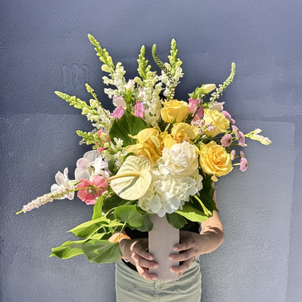 Mixed bouquet of yellow, white, and pink flowers in a tall vase