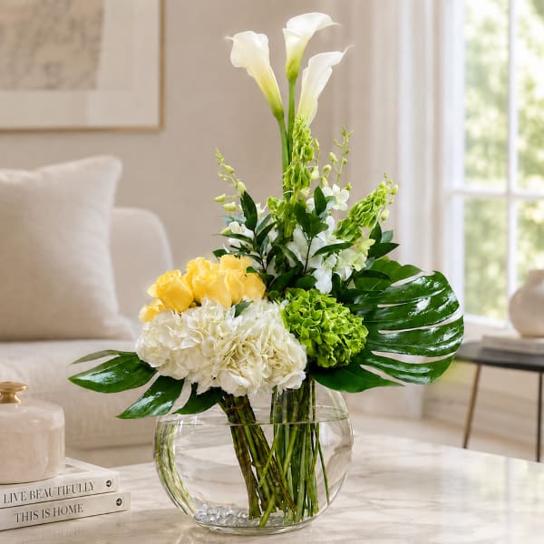 White calla lilies, yellow roses, and green hydrangeas in a glass vase.