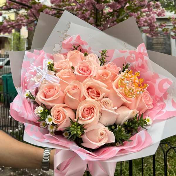 Peach rose bouquet wrapped in pink paper with a decorative crown accent.