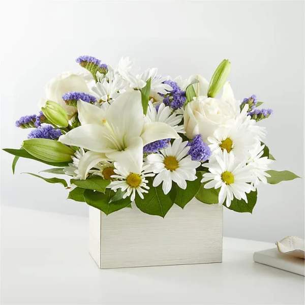White lilies and daisies arranged in a square white box with purple accents
