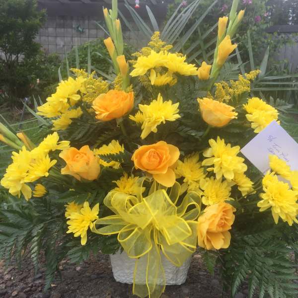 Yellow and orange flowers arranged in a white container with a yellow bow.