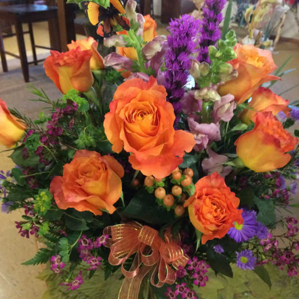 Orange roses and purple flowers in a glass vase with a ribbon