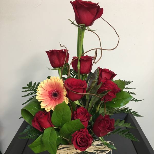 Red roses and a peach gerbera daisy in a clear glass vase