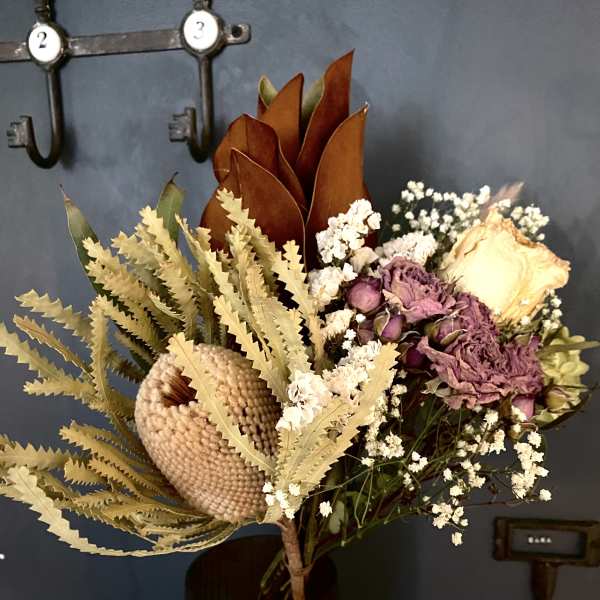 Dried floral bouquet in an amber glass vase with cream and purple blooms
