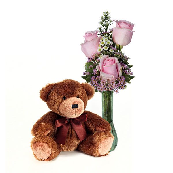 Pink rose bouquet in a glass vase beside a brown teddy bear