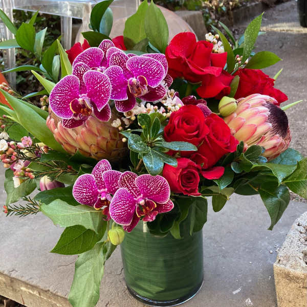 Bouquet of red roses and purple orchids in a green glass vase