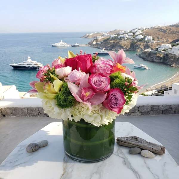 Pink and white flower arrangement in a glass vase on a table by the sea