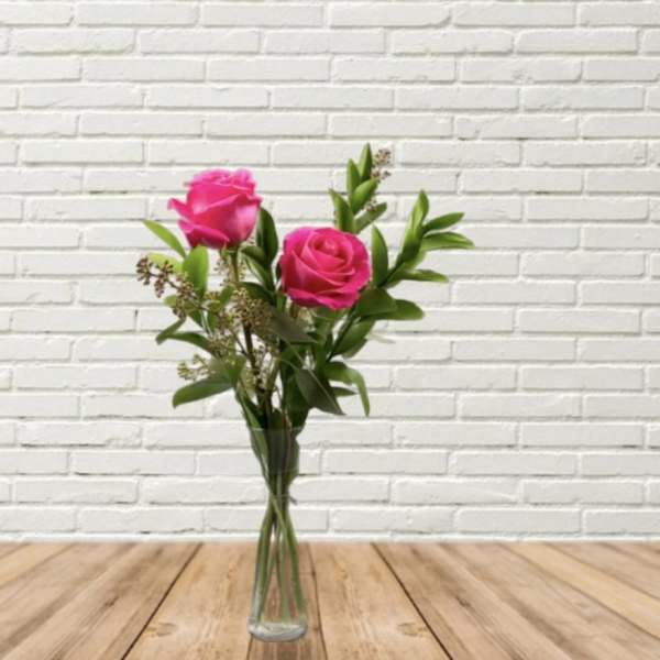Two pink roses in a clear glass vase with greenery