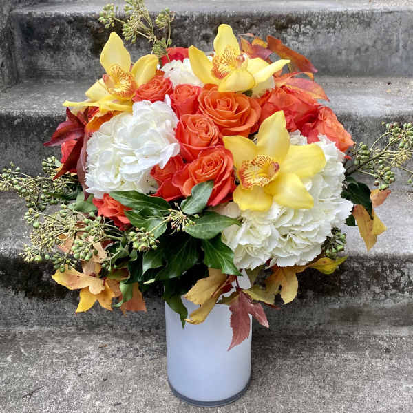 Bouquet of orange roses, white hydrangeas, and yellow orchids in a white vase