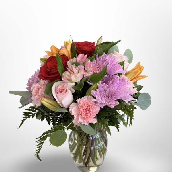 Mixed bouquet of roses, lilies, carnations, and chrysanthemums in a glass vase
