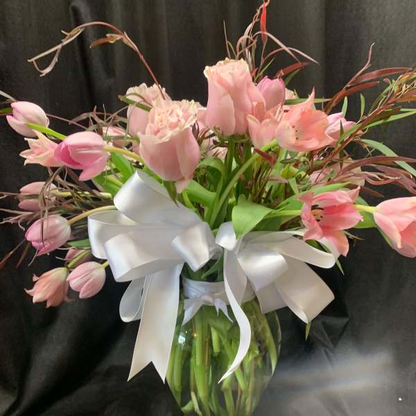 Pink tulips and roses in a glass vase with a white ribbon
