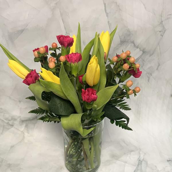 Yellow tulips and pink carnations in a clear glass vase