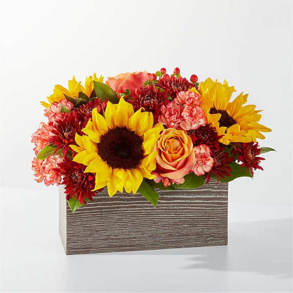 Sunflowers, roses, and carnations arranged in a striped rectangular box
