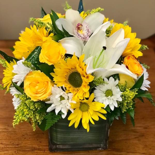 Yellow and white mixed flower arrangement in a square glass vase