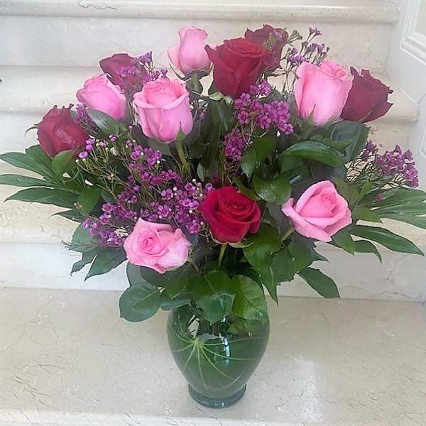 Arrangement of pink and red roses with small purple flowers in a green glass vase
