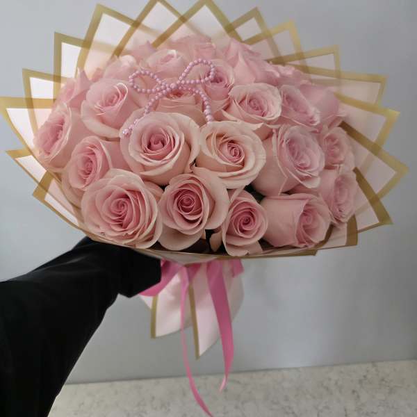 Bouquet of pale pink roses wrapped in gold-edged paper with a pink ribbon