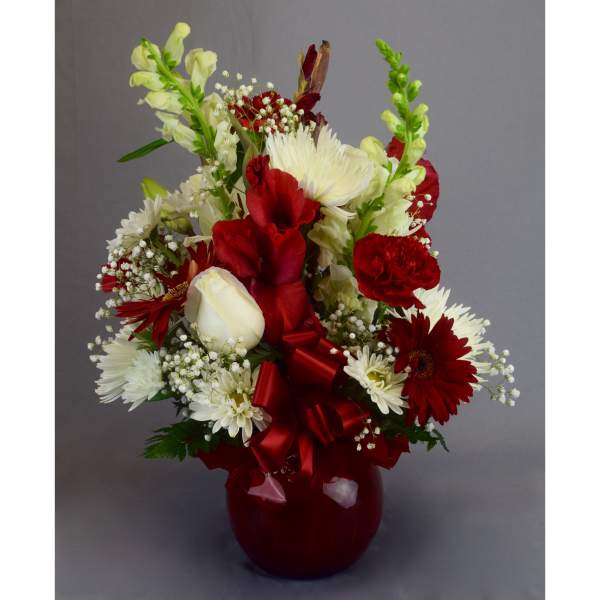 Red and white mixed flower arrangement in a red vase with a ribbon