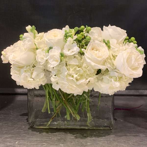 White roses and hydrangeas arranged in a clear rectangular vase