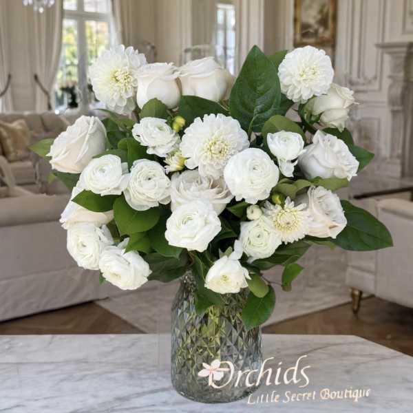 White roses and ranunculus in a glass vase with green leaves